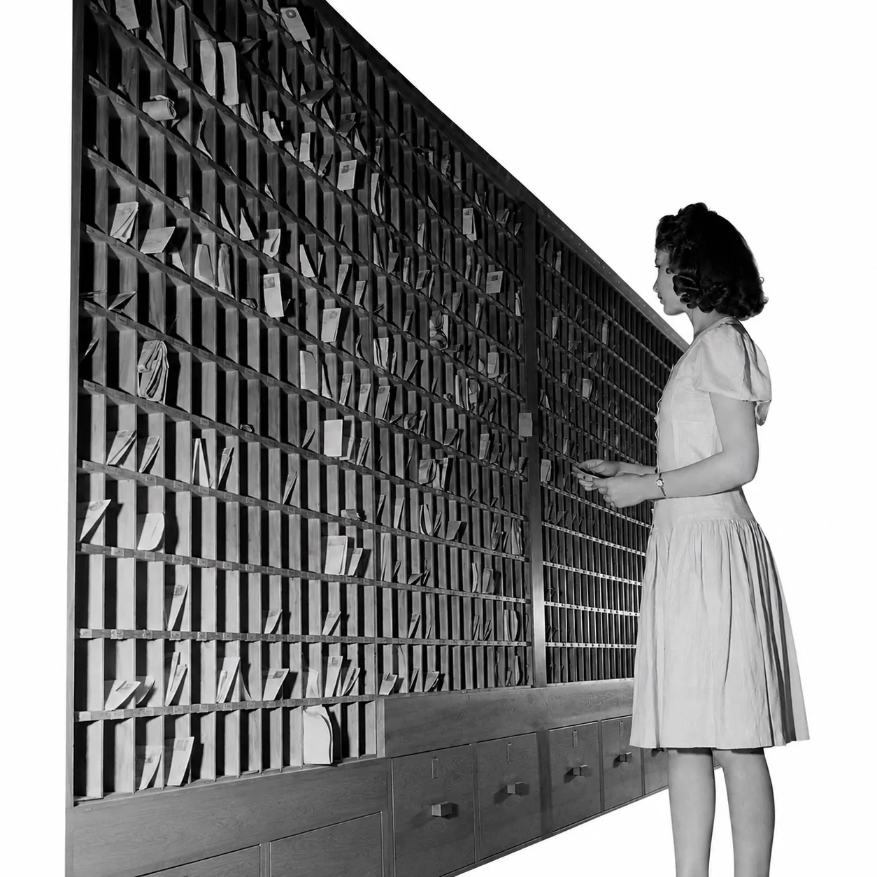 An archive photograph of a clerk at a wall of pigeonhole
                  card files.
